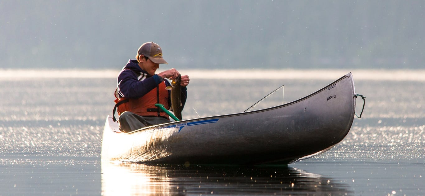 man catching fish in canoe on lake