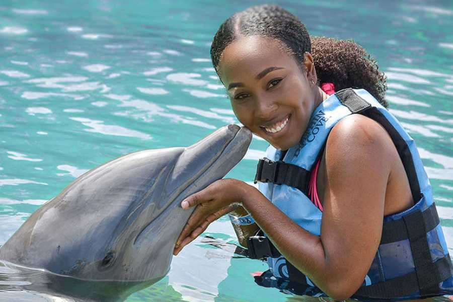 A joyful encounter between a woman and a playful dolphin in sparkling blue water.