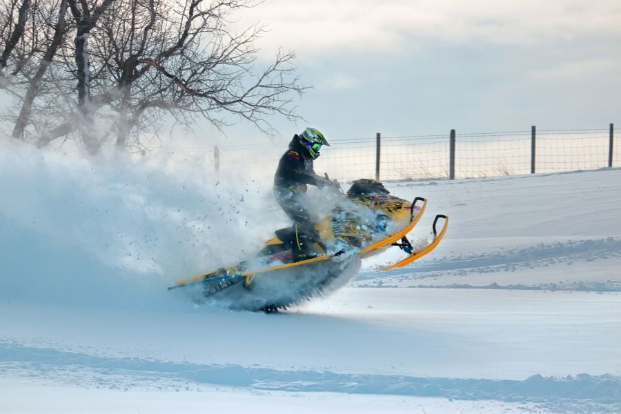 Snowmobiler carves through deep powder, sending snow flying high.