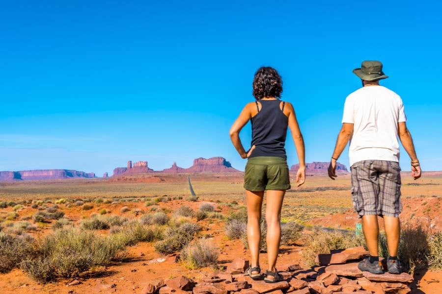 Two hikers admire Sedona’s red rock towers under a wide, clear blue sky.