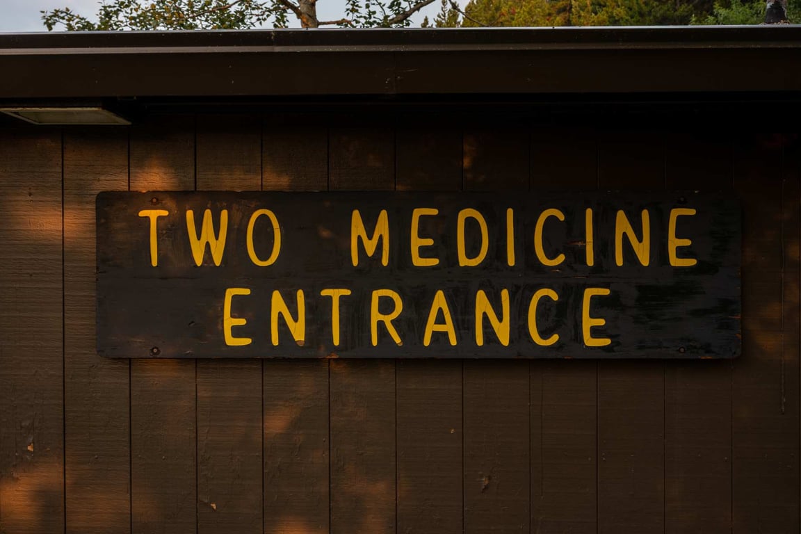 sign that reads "two medicine entrance" in yellow letters