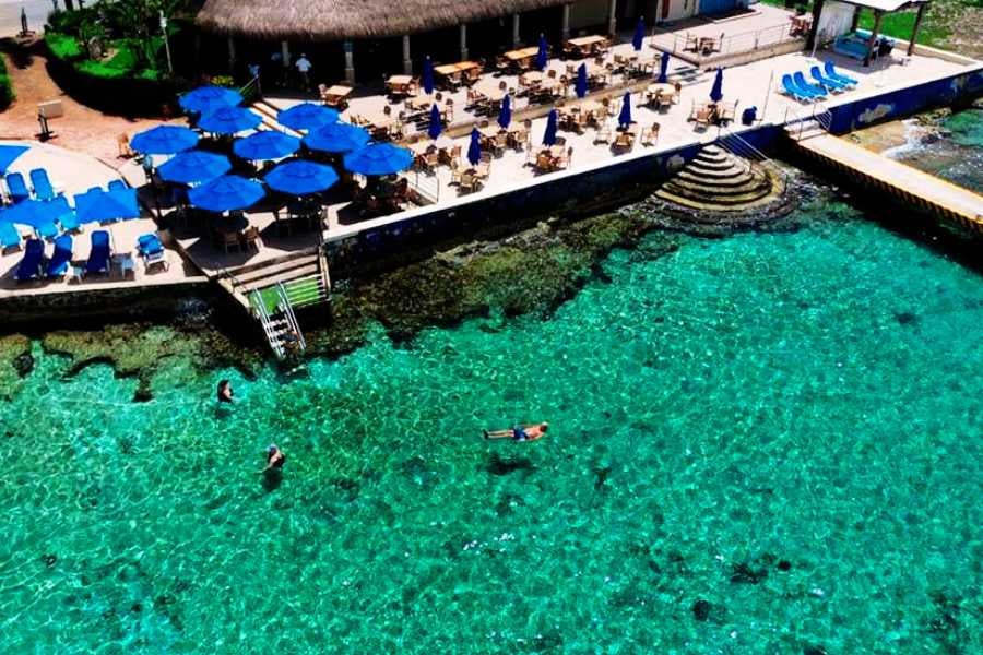 Swimmers float in turquoise waters near a lively beachside restaurant, perfect for snorkeling and relaxation.