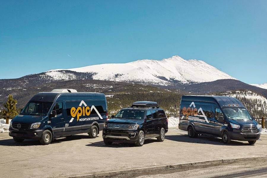 Vans and an SUV parked with snow-capped mountains behind them.