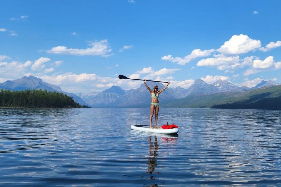 A woman celebrates while paddleboarding on a calm mountain lake.