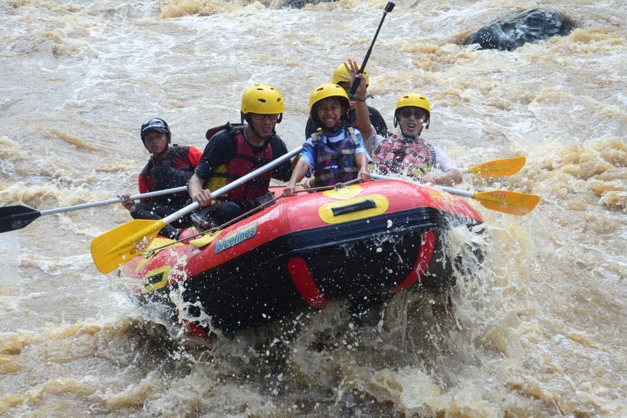 Family rides bumpy muddy rapids, gripping paddles with big grins.