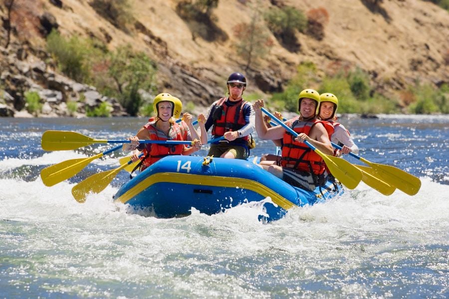 Friends paddle hard while rafting through splashing river rapids.