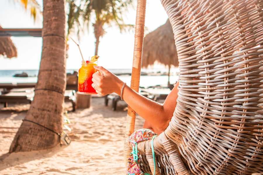 A peaceful scene of a beachgoer sipping a vibrant tropical drink in a cozy wicker chair by the sea.