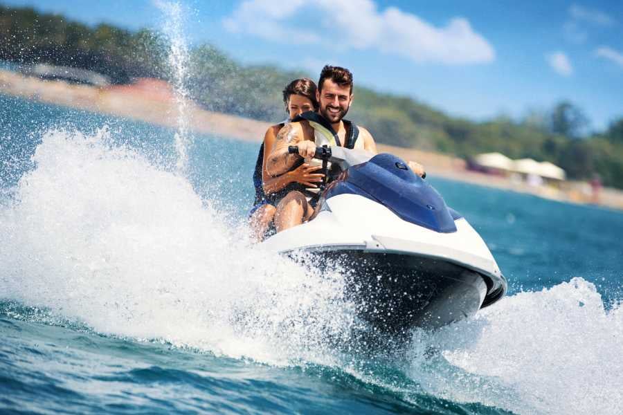 A couple laughs as they ride a jet ski, splashing through crystal-clear waters under the sun.