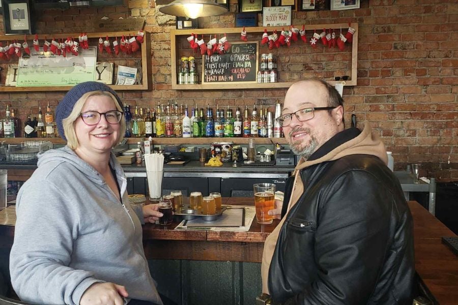 A couple shares a tasting flight and beer at a rustic indoor bar.