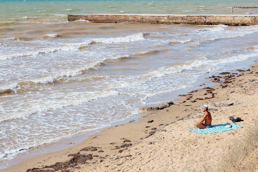 A quiet beach with soft waves and someone relaxing on a towel under the sun.