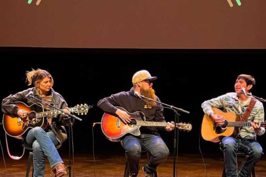 Three singers play guitars and share songs at a live show.