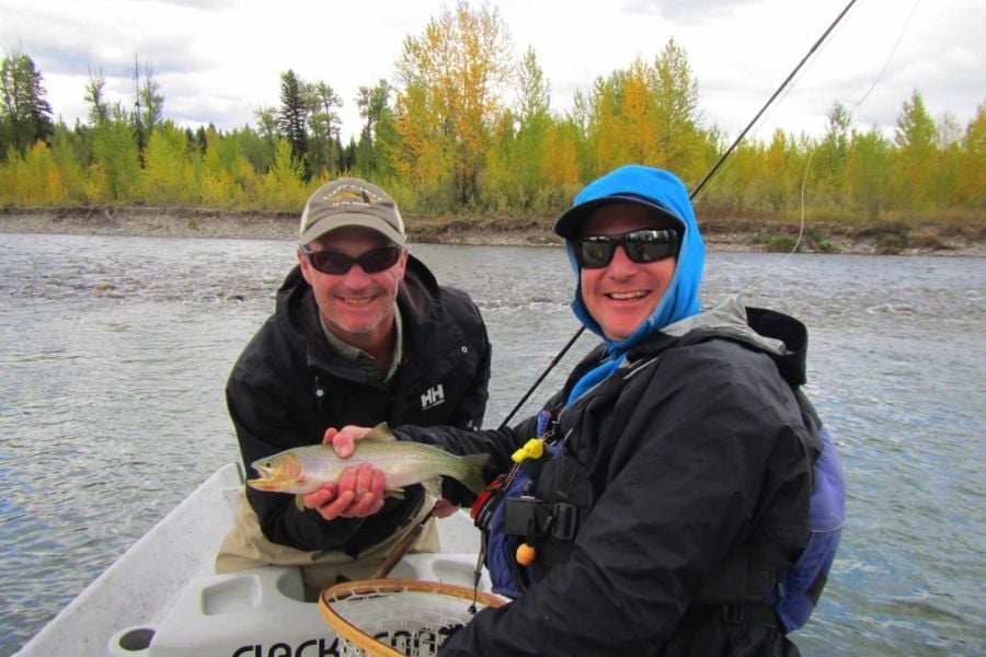 Two friends smiling proudly while showing off their fresh catch on the river.