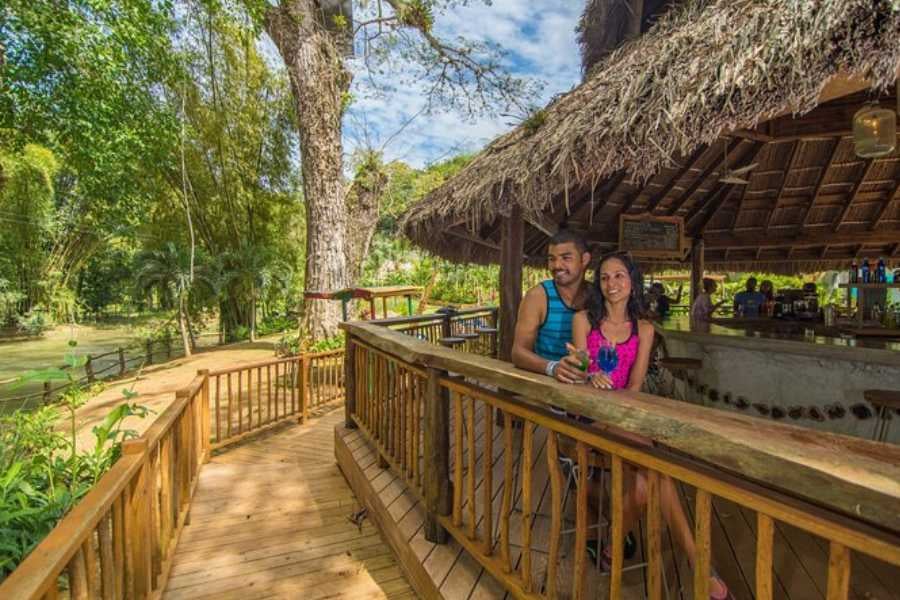 A couple relaxes at a tropical riverside bar, soaking in the peaceful jungle vibes and refreshing drinks.