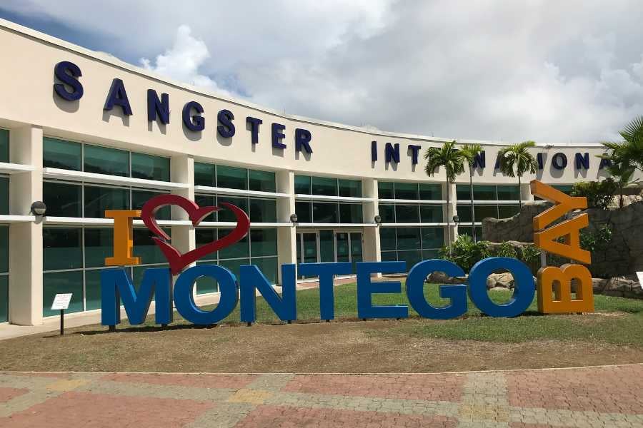 A sunny exterior shot of Sangster International Airport, featuring the "I Love Montego Bay" sign.