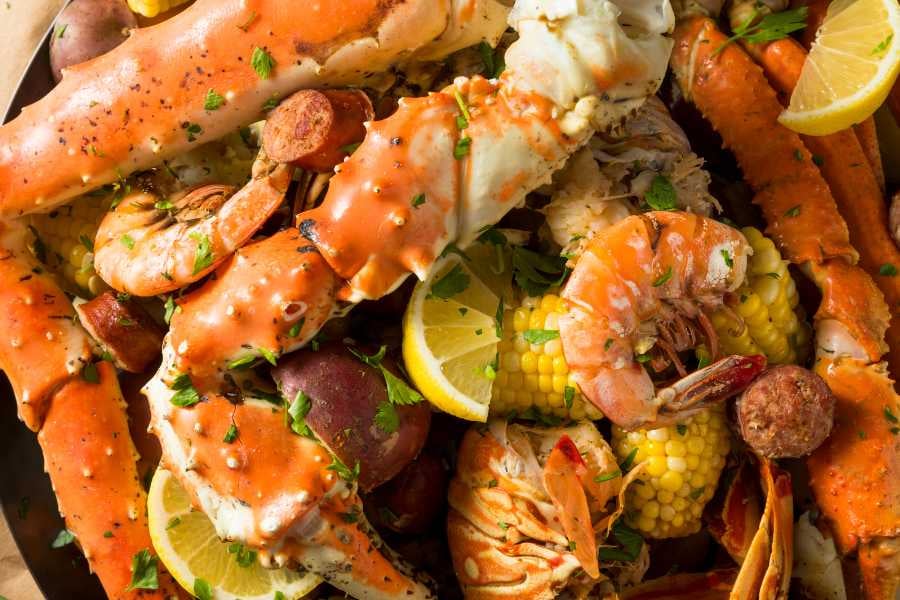 A seafood dish with crab, shrimp, corn, and potatoes, topped with herbs and lemon slices.