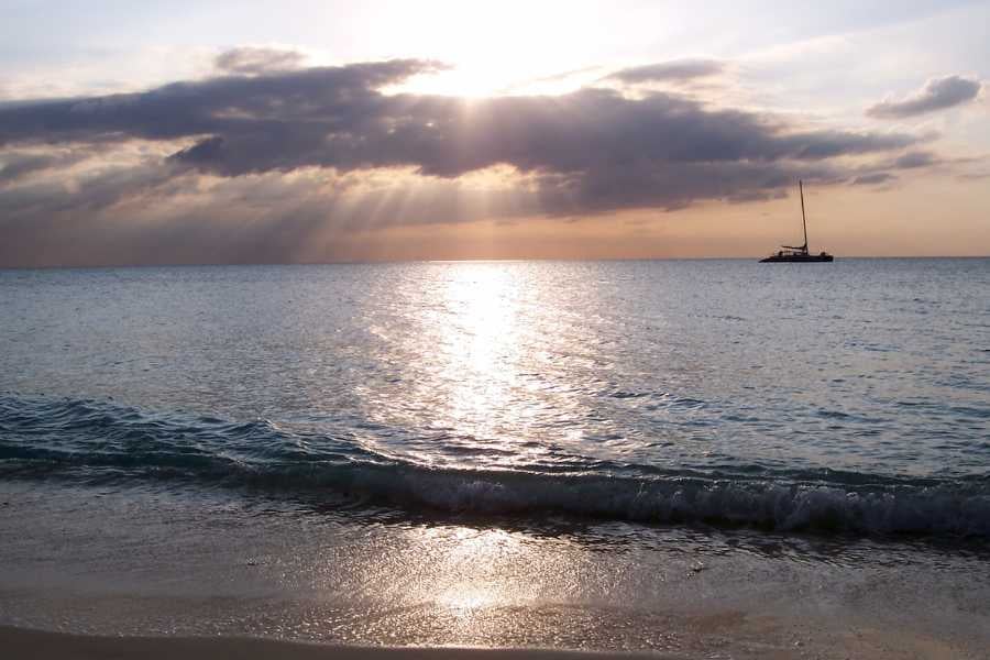 A tranquil ocean at sunset with a sailboat in the distance, creating a peaceful, dreamy scene.