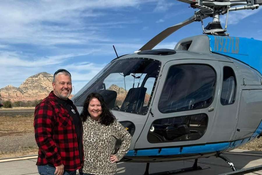 A couple poses in front of a helicopter before taking off on an adventure.