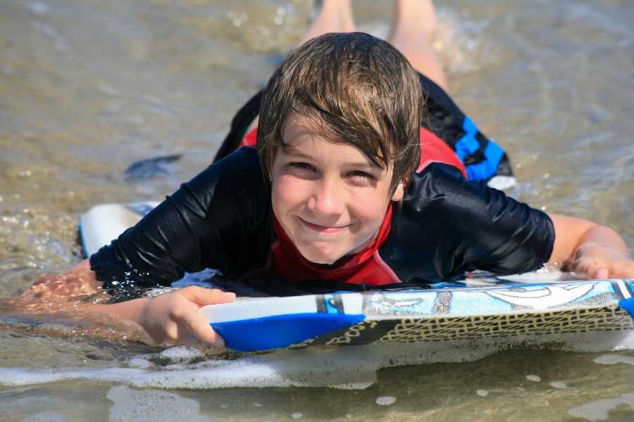 A boy enjoys the waves while surfing on a bodyboard at the beach, smiling brightly.