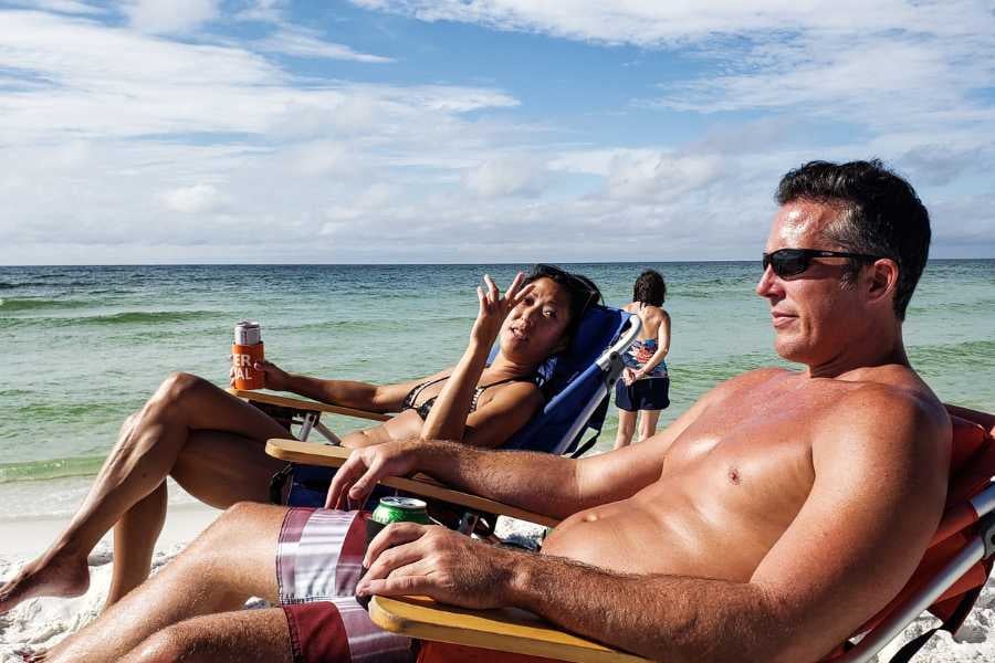 A couple relaxes on beach chairs, enjoying drinks while soaking up the sun and ocean breeze.