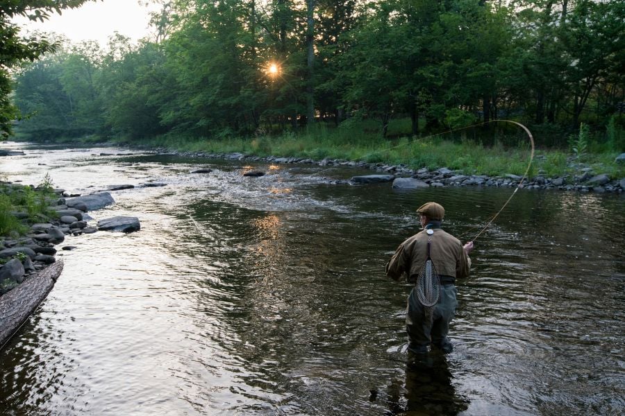 An angler casts a line in a calm river at sunrise.