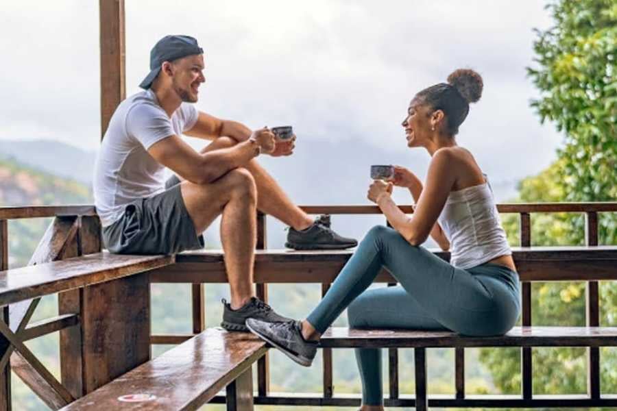 A couple sips coffee on a scenic wooden deck, surrounded by lush mountains and fresh morning air.