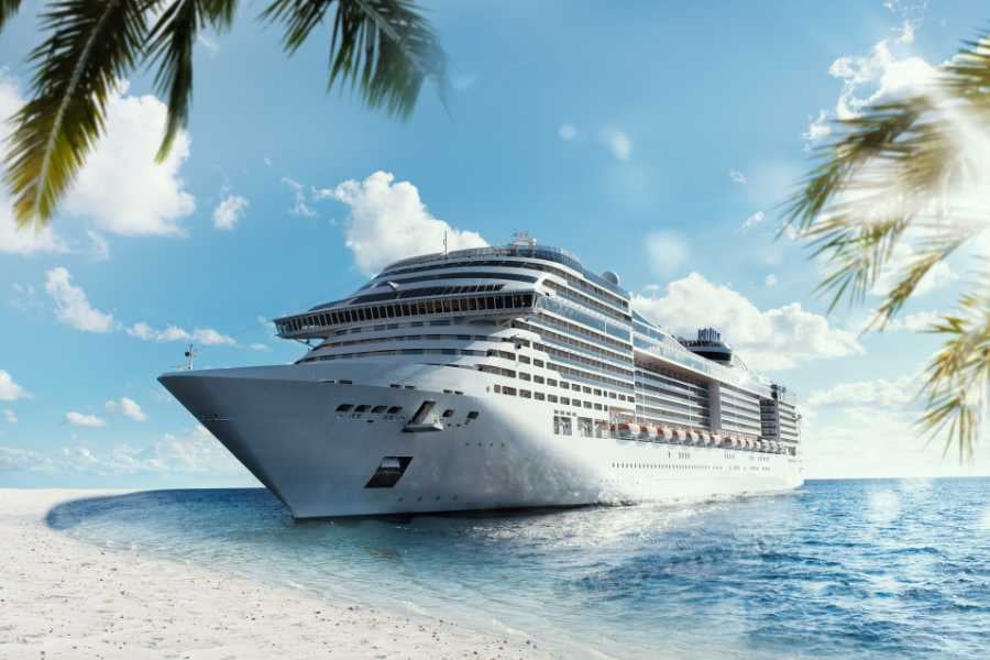 A big cruise ship near a sandy beach with palm trees and a clear blue sky.