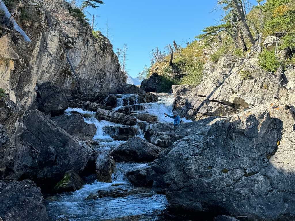 man fishing in creek with gentle waterfall