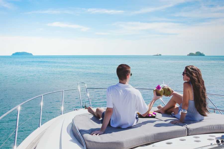 A couple relaxes on a yacht, clinking coconuts while surrounded by the endless blue sea and sky.