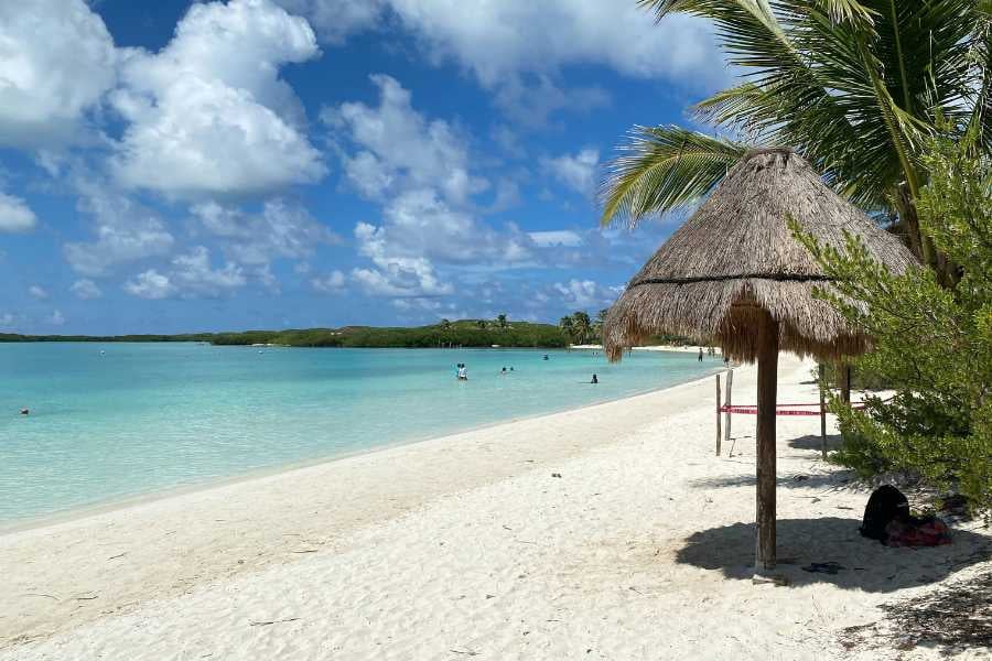 A peaceful beach with soft white sand, palm-thatched umbrellas, and calm turquoise water under a bright blue sky.