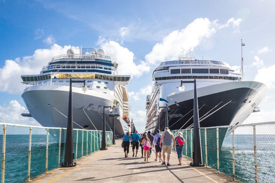 Cruise passengers walking down the pier between two huge ships.