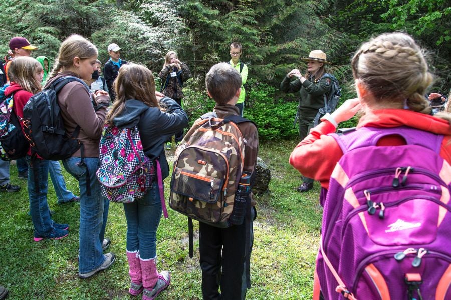 Children listen to a park ranger explaining nature in a green meadow.