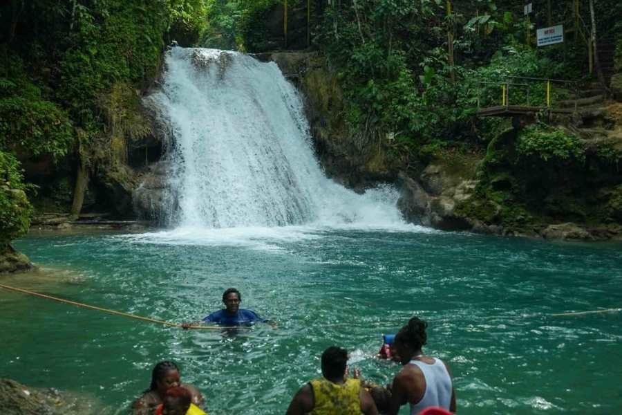 Visitors swim and explore a stunning waterfall, surrounded by thick jungle and clear, refreshing turquoise water.