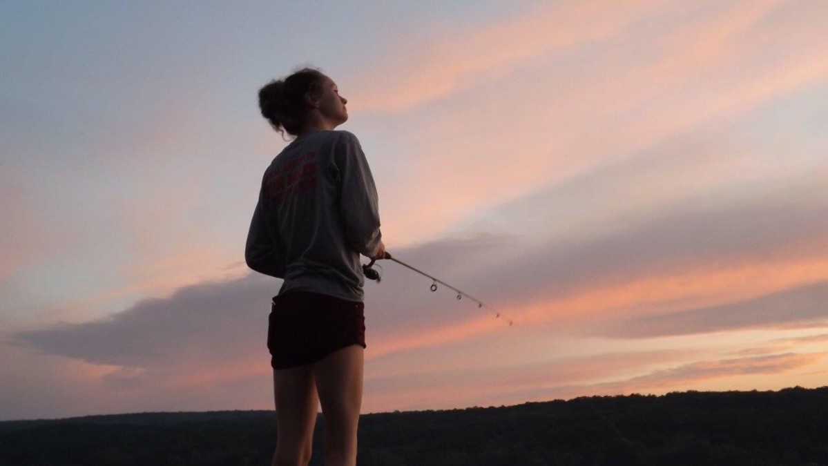 woman fishing on lake at sunset