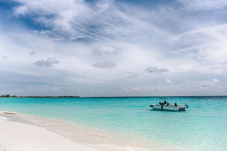 A boat gently floats on calm, clear waters with a beautiful beach backdrop in the distance.