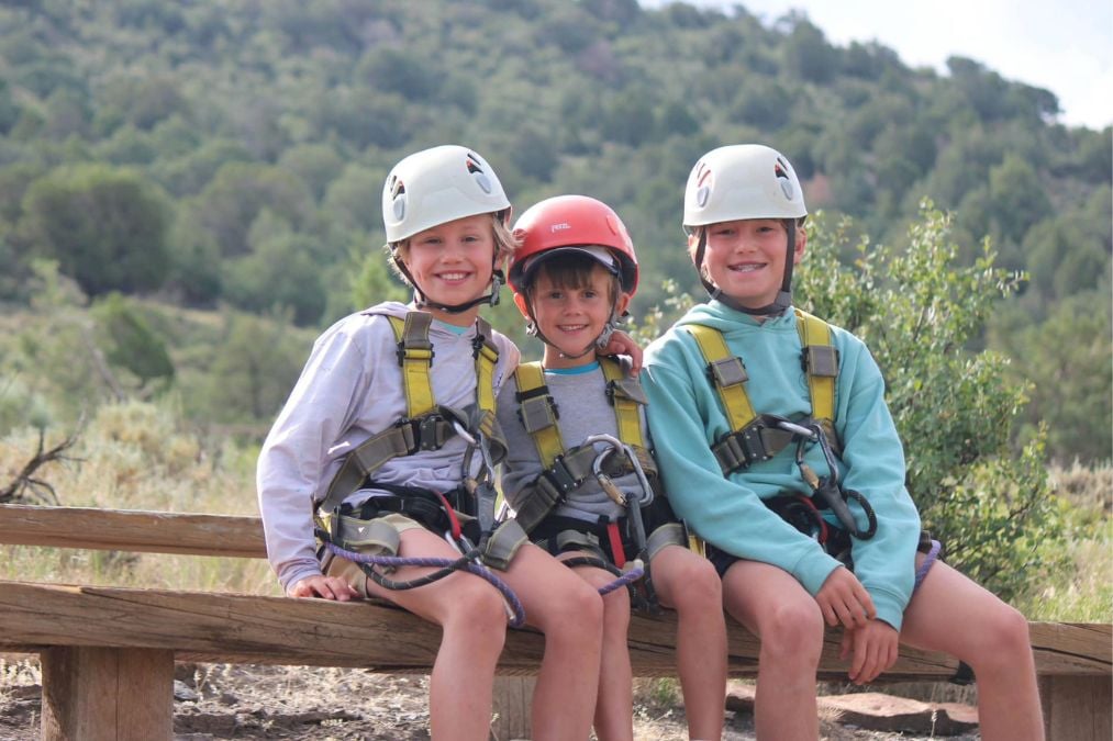 Three smiling kids in helmets get ready for a Breckenridge outdoor adventure.