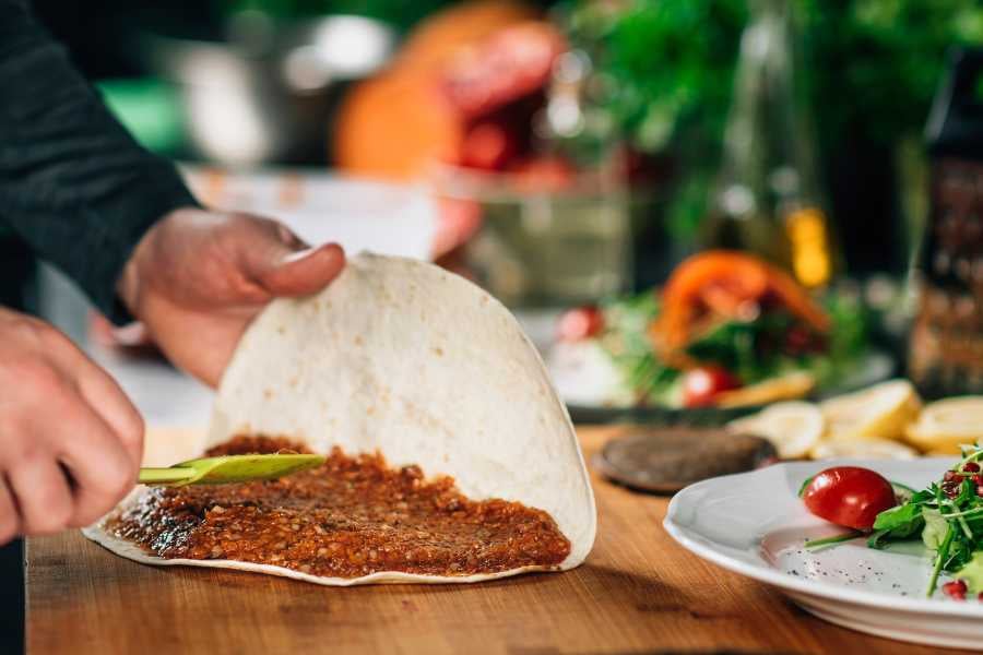 Hands spreading a savory filling on a tortilla, preparing a fresh and flavorful dish in a lively kitchen.