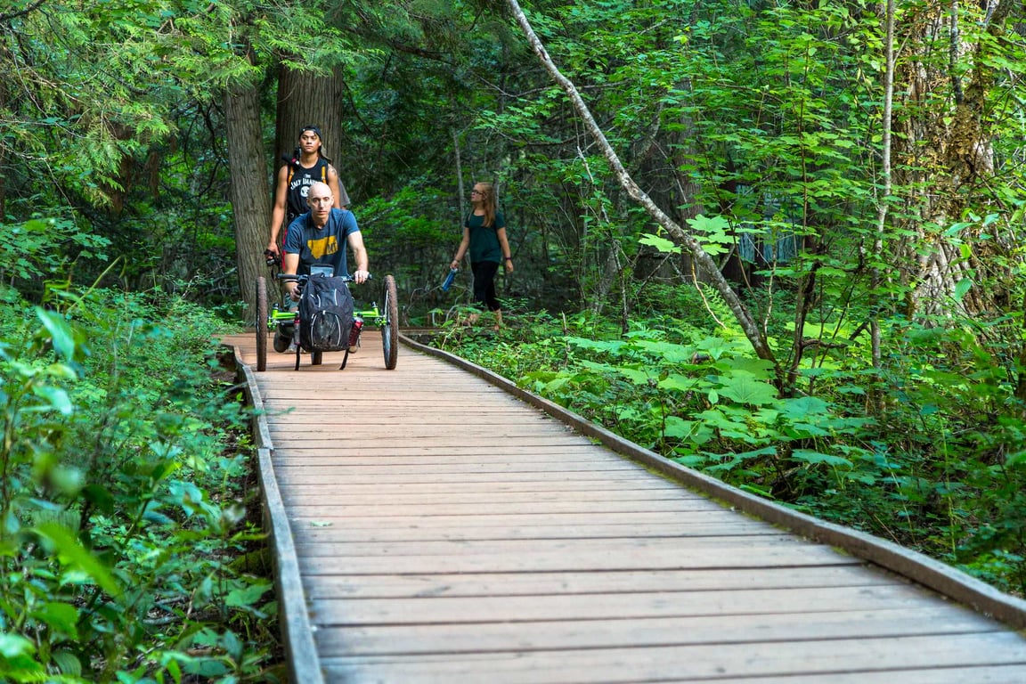 man in off-road wheelchair crossing cedar boardwalk in forest