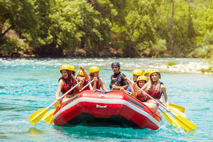Group rafting down a bright blue river, paddles splashing water.