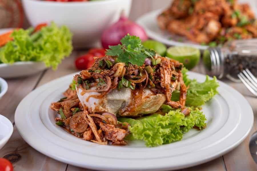 A beautifully garnished plate of spicy fish topped with herbs and vegetables, ready for a delicious meal.