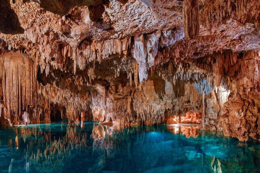 A breathtaking underground cave with shimmering turquoise waters and stunning stalactites hanging from above.