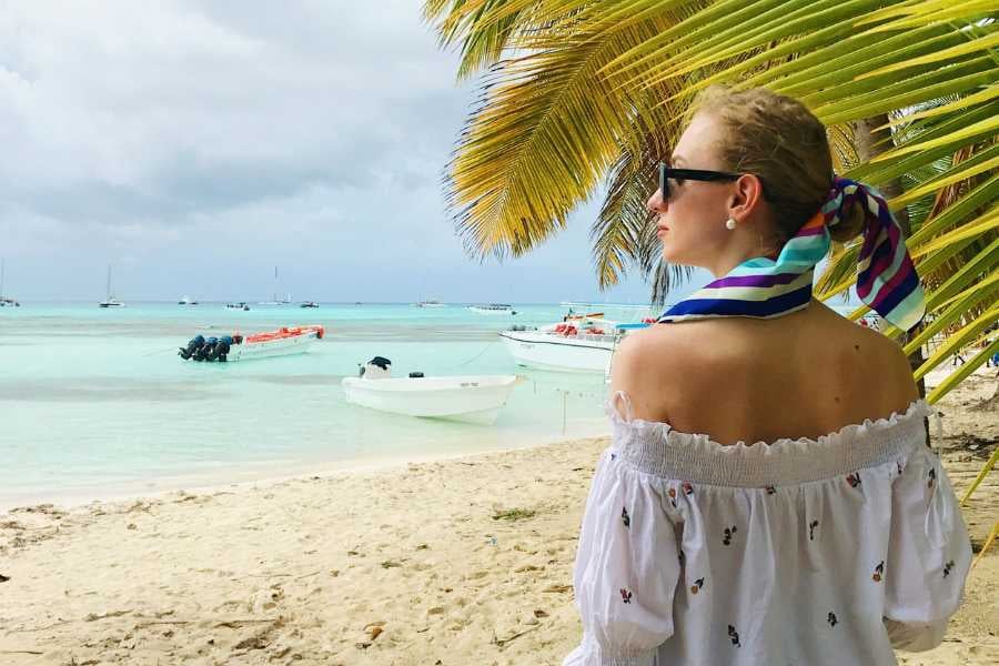 A woman enjoys the beach breeze while gazing at the boats near a tropical shoreline.