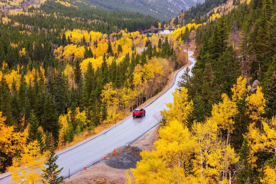 A red car drives through golden autumn trees in the mountains.