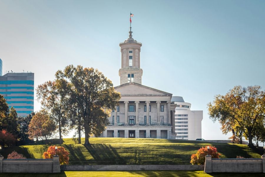The Tennessee State Capitol sits proudly on a grassy hill with trees all around.
