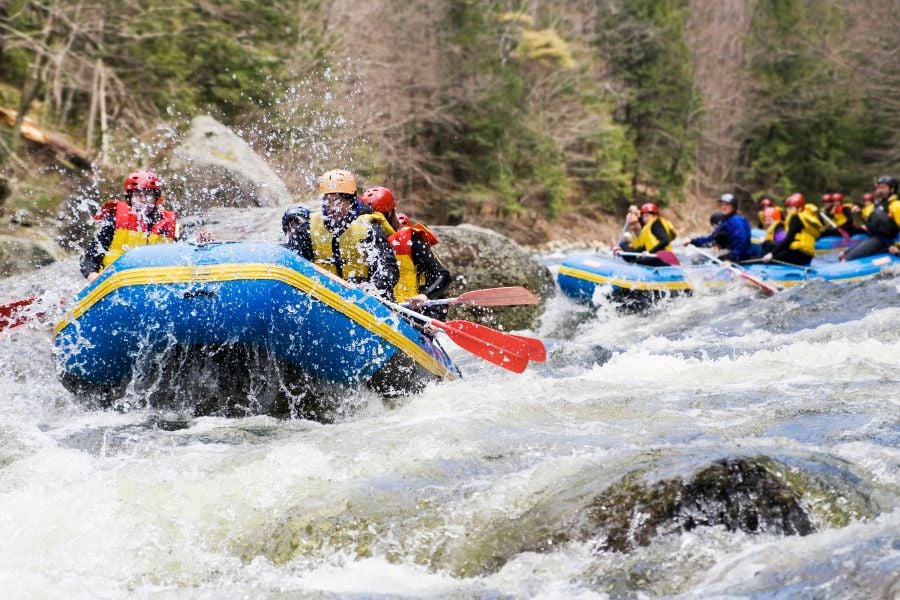 Several rafts rush through choppy whitewater, splashing as they hit the waves.