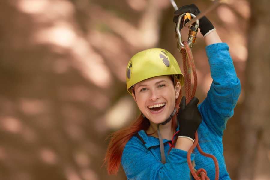 A cheerful zipliner gliding through a lush forest, wearing a helmet and harness with a big smile.