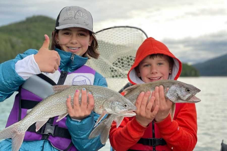 Kids proudly hold up their fresh catch, smiling with excitement on a fishing trip.