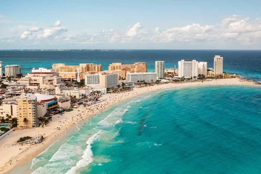 Cancun's vibrant beachfront with clear waters and bustling resorts under a sunny sky.