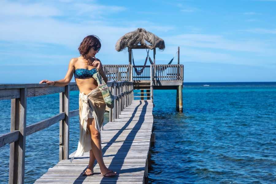 A women enjoys a scenic stroll along a wooden pier, gazing at the turquoise ocean.