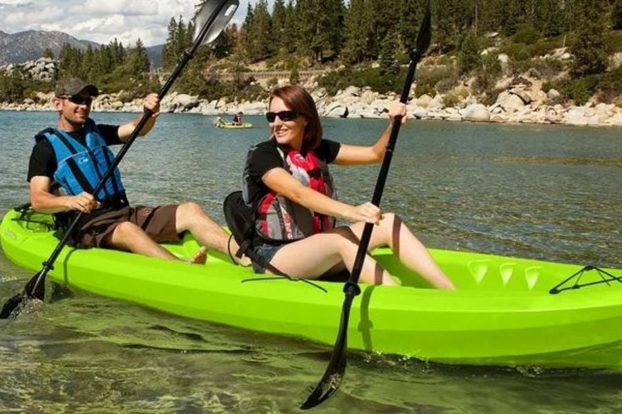 A couple kayaks across clear blue water, smiling as they paddle together under the sun.
