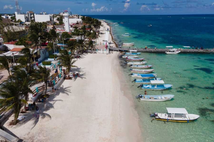 Fishing boats lined along a serene coastline with soft sands and crystal-clear blue waters, perfect for a tranquil day.